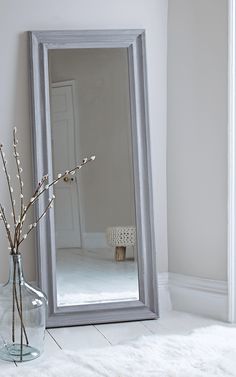 a large mirror sitting on top of a floor next to a vase filled with flowers