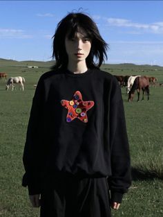 a woman standing in front of horses wearing a black sweatshirt with colorful stars on it