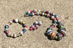 two bracelets made out of rolled up paper beads on the ground, one is shaped like a heart