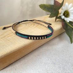 a bracelet that is sitting on top of a piece of wood next to a flower