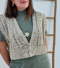 a woman standing in front of a ladder wearing a knitted sweater and green skirt