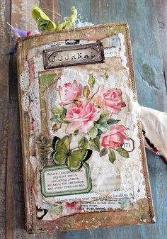 an altered book with pink roses and butterflies on it, sitting on a wooden surface