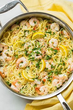 a pan filled with pasta and shrimp on top of a yellow table cloth next to lemon wedges