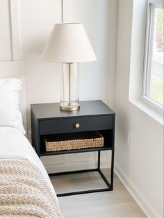 a nightstand with a basket underneath it and a lamp on the end table next to it