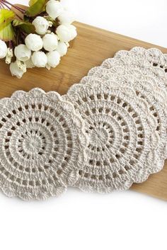 four crocheted doily sitting on top of a wooden cutting board next to flowers