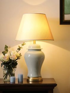 a white vase sitting on top of a wooden table next to a lamp and flowers