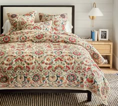 a bed with a colorful comforter on top of it in a room next to a lamp