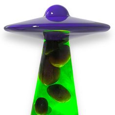 a green and purple vase with olives in it on a white surface, next to an alien like object