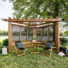 a wooden pergolan with two chairs and a table in the grass next to it