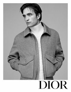 a man wearing a coat and sweater standing in front of a gray background with the words dior on it