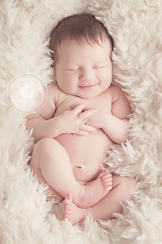 a baby is smiling while laying down on a fluffy white blanket with his eyes closed