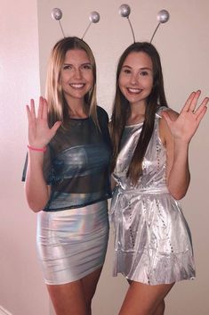 two girls dressed in silver posing for the camera with their hands up and fingers out