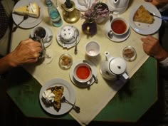 people sitting at a table with plates and cups of tea, cake and desserts