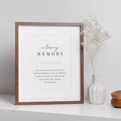 there is a vase with flowers next to a framed memory print on a shelf in front of a white wall