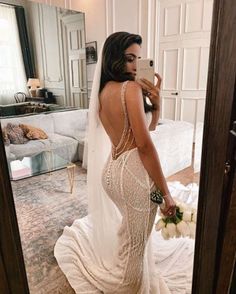 a woman in a wedding dress taking a selfie with her cell phone while looking at herself in the mirror