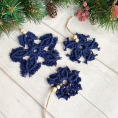 three crocheted snowflakes hanging from a christmas tree with pine cones in the background