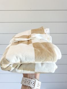 a woman's hand holding two blankets on top of each other in front of a white wall