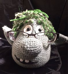 a crocheted stuffed animal wearing glasses on top of a black surface with green hair and eyeglasses