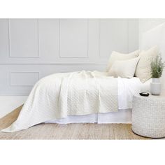 a bed with white sheets and pillows on top of it next to a plant in a vase