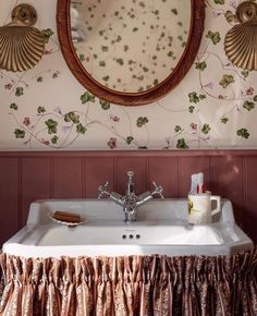 a bathroom sink under a mirror next to a wallpapered wall with flowers on it