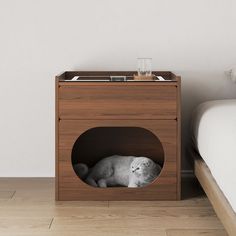 a cat is laying in a small wooden box on the floor next to a bed