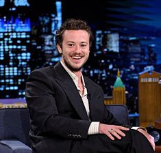 a smiling man in a suit sitting on a chair