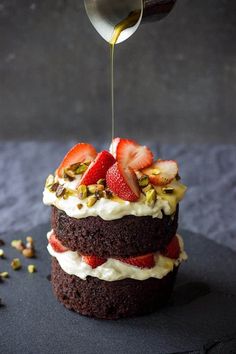 someone drizzling strawberries on top of a chocolate cake with white frosting