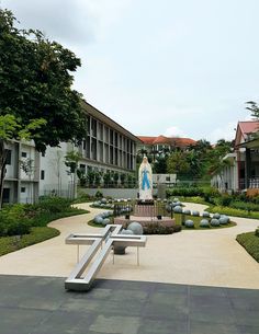 a statue in the middle of a courtyard with benches and trees around it, surrounded by buildings