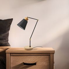 a nightstand with a lamp on it next to a brown pillow and black throw pillows