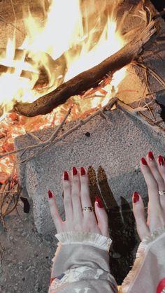 a woman with red nails standing in front of a fire