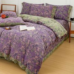 a bed covered in purple and green bedspreads on top of a wooden floor