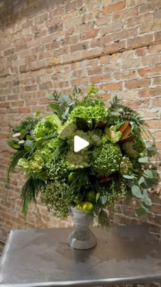 a vase filled with lots of green flowers on top of a metal table next to a brick wall