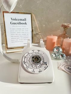 an old fashioned white telephone sitting on top of a table next to candles and a sign