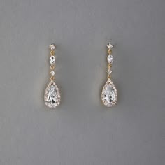 two pairs of diamond earrings on a gray surface with one pair dangling from the side