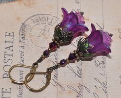 two purple flowers are attached to antique brass hooks on a piece of paper with writing in the background