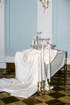 a table covered with white cloth next to two candles on top of a checkered floor