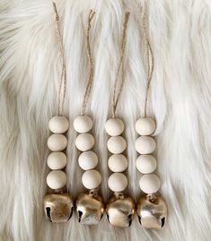 three wooden bells are hanging on a white fur covered surface with gold and silver beads