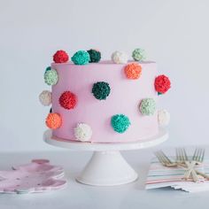 a pink cake decorated with pom - poms on a white pedestal next to other decorations