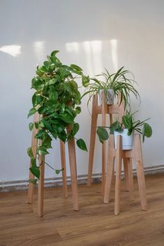 three wooden plant stands with plants in them on the floor next to a white wall