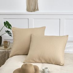 two pillows and a hat on a bed with a plant in the corner next to it