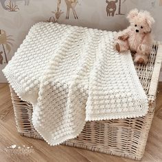 a teddy bear sitting on top of a wicker basket next to a crocheted blanket