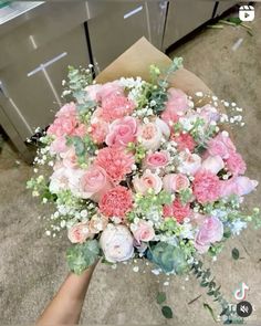 a bouquet of pink and white flowers is held by someone's hand in front of an oven