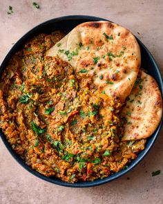 a bowl filled with bread and vegetables next to pita bread on top of a table