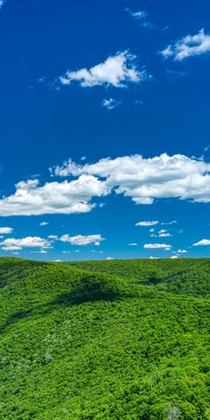 an aerial view of a lush green hillside under a blue sky with white fluffy clouds