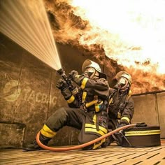 two firemen in protective gear are spraying water on the floor while another man looks on