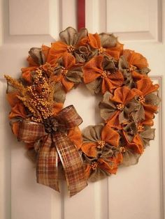 an orange and brown wreath hanging on the front door with burlocked ribbon