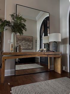 a large mirror sitting on top of a wooden table in front of a window next to a plant