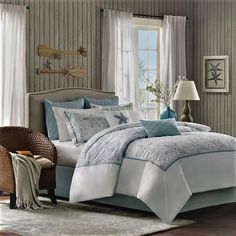 a bed with white and blue comforters in a bedroom next to a chair, lamp and window