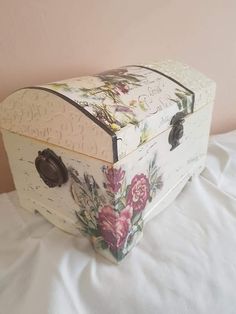 an old fashioned box with flowers painted on it sitting on a white sheet covered bed