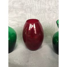 three red and green vases sitting next to each other on a white tablecloth